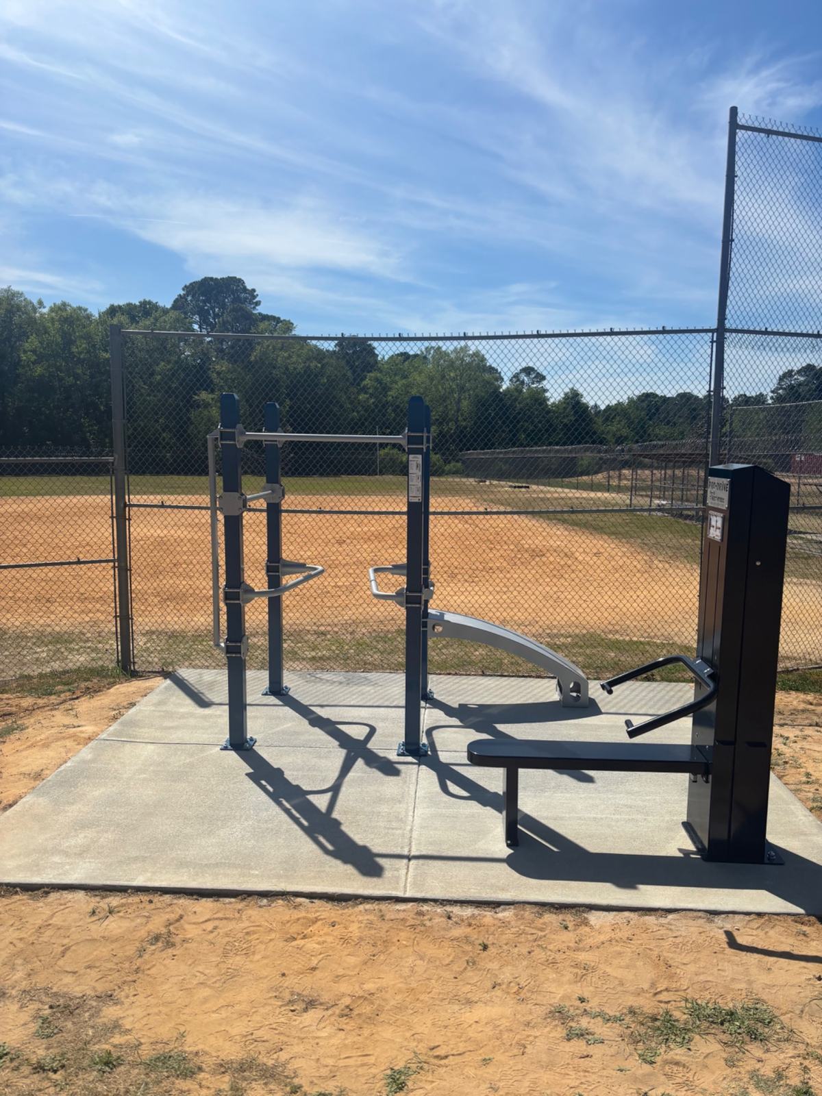 Corrections-Fit calisthenics equipment anchored to a concrete pad in a fenced outdoor recreation yard. 